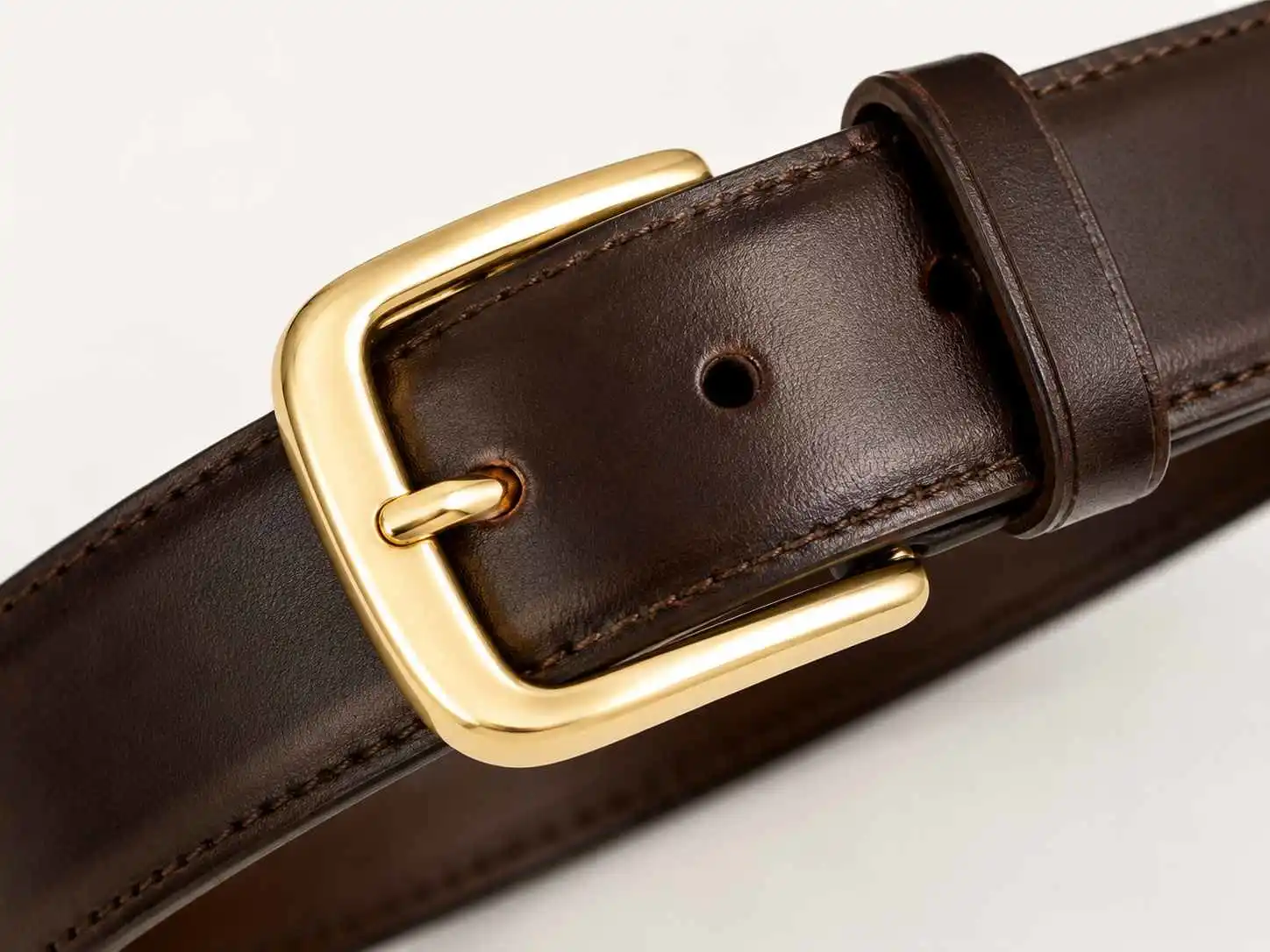 metal buckle belt, A polished gold metal buckle is attached to a dark brown leather belt with adjustment holes and a leather keeper.